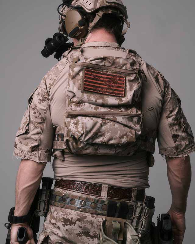 Seen from behind, a service member in desert digital camouflage and a plate carrier wears a hand-tooled leather belt below the rig.