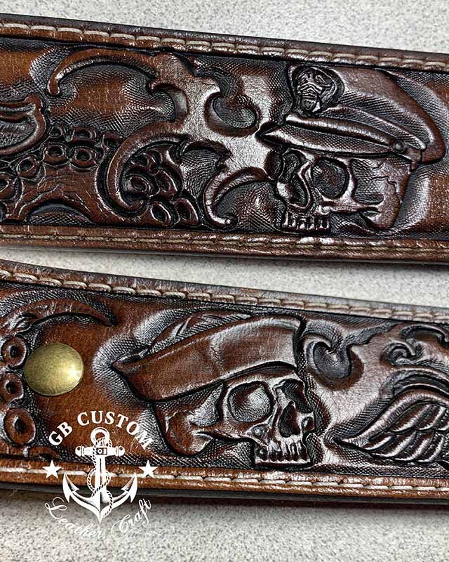 Two sections of a dark brown belt laid side by side, each tooled with a skull in a peaked officer's cap surrounded by scrollwork.